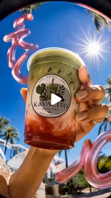 A hand raising a strawberry matcha in a Kavacito cup against palms and blue sky