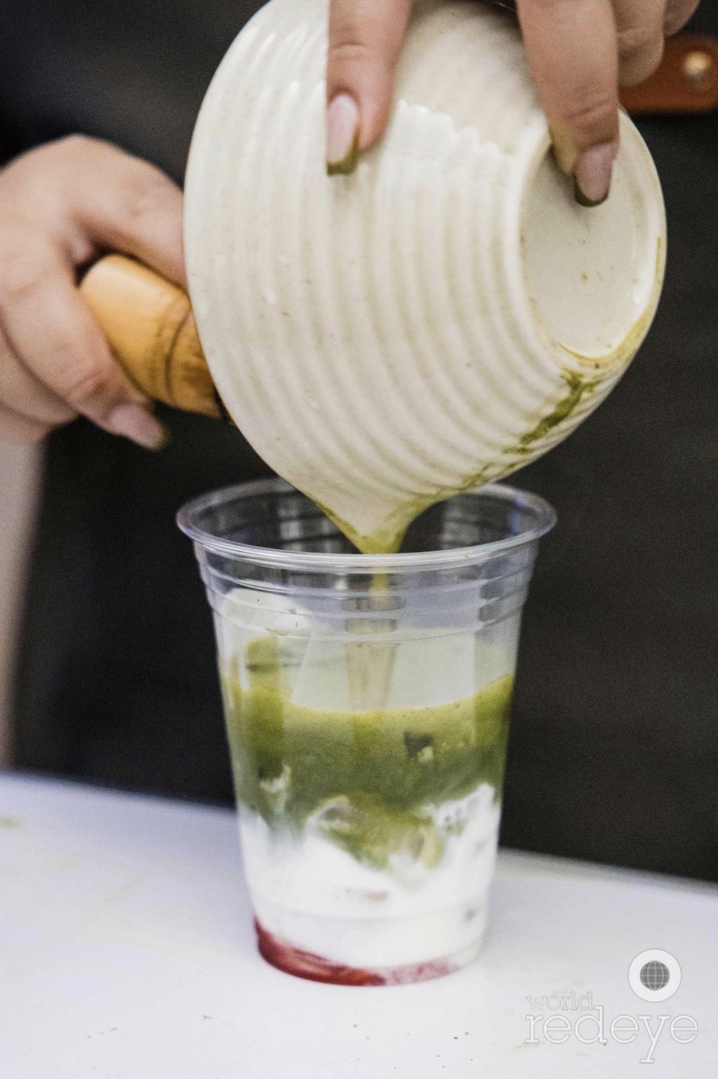 Ceremonial matcha poured from a whisking bowl into an iced cup of milk